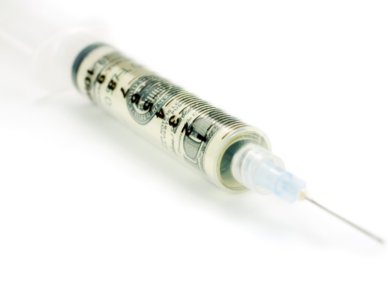 A syringe containing a rolled-up U.S. hundred-dollar bill instead of liquid, symbolizing the concept of money in healthcare or the high costs of medical treatment.